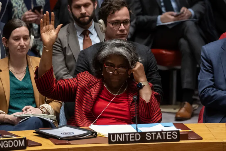 A woman wearing a red suit and red glasses raises her hand to vote behind a plaque saying United States