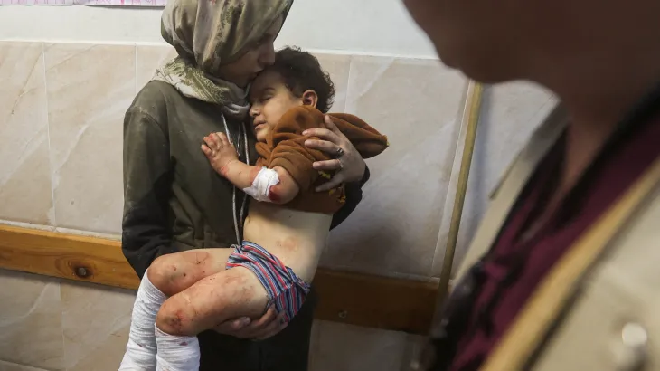 A Palestinian woman holds a child wounded in an Israeli strike