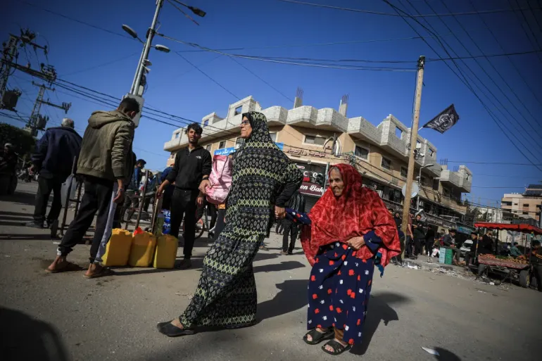 A woman helps an elderly woman walking on foot during the evacuation from Bureij to Deir el-Balah, which has been hit in Israeli raids. [Abdelhakim Abu Riash/Al Jazeera]