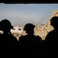 Four IDF soldiers look out a window at a partially demolished neighborhood in the Gaza Strip, in a handout photo released December 18, 2023. (Israel Defense Forces)