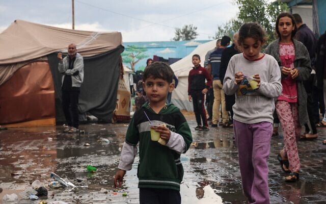 Internally displaced Palestinian children living in a school run by the UN agency for Palestinian refugees (UNRWA), walk across a wet courtyard following overnight rainstorms in Rafah in the southern Gaza Strip on November 15, 2023, during the Israel-Hamas war. (SAID KHATIB / AFP)