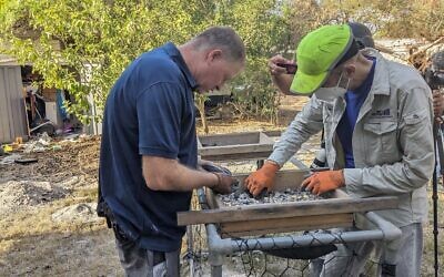 Oren Shmueli, left, and Hai Ashkenazi sift through material from a burned home in Kibbutz Nir Oz, looking for remnants that can help identify victims on November 9, 2023. (Melanie Lidman/Times of Israel)