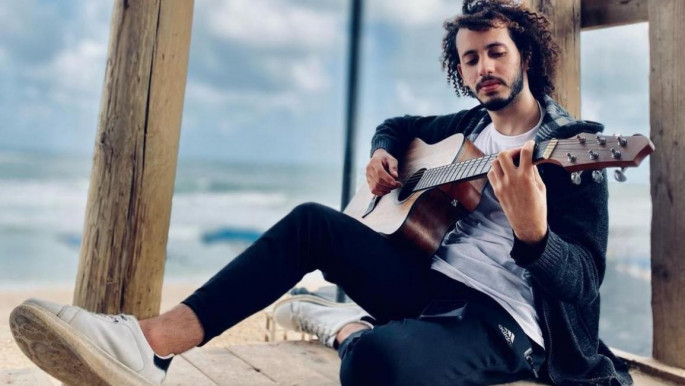 Young man with guitar sitting hear the sea